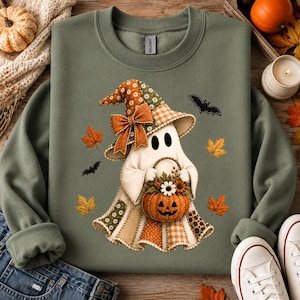 Peut inclure: Un sweat-shirt à col rond vert olive orné d'un motif représentant un fantôme portant un chapeau de sorcière en patchwork et tenant un panier citrouille rempli de fleurs. Le design inclut des feuilles d'automne orange et deux chauves-souris.