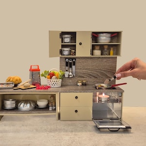 Puede incluir: Mini cocina con armarios beige, encimera de madera y horno pequeño. Incluye cesta de verduras, utensilios de cocina y sartén. Se muestra una mano usando una espátula en la sartén.