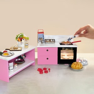 以下が含まれることがあります： 白いカウンタートップを備えたミニチュアピンクのキッチンセット。コンロ、オーブン、小さな島があります。セットには、野菜のバスケット、食べ物が入ったフライパン、ケーキが含まれています。手はヘラを持っています。