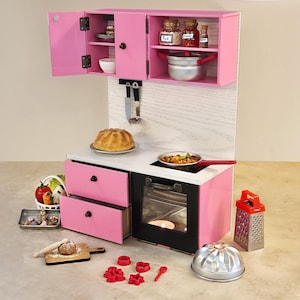 K&ouml;nnte beinhalten: Eine rosa Spielzeugk&uuml;che mit Herd, Backofen und Schr&auml;nken. Zubeh&ouml;r umfasst einen Kuchen, eine Pfanne mit Essen, eine Reibe und Backutensilien. Das Set ist f&uuml;r Kinderspiele und fantasievolles Kochen konzipiert.