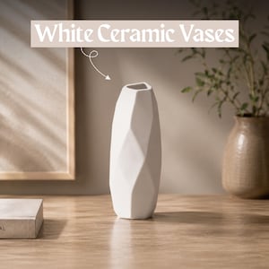 Può includere: Un vaso in ceramica bianca con una superficie geometrica sfaccettata e un'apertura stretta. Il testo "White Ceramic Vases" è visualizzato sopra l'oggetto, accompagnato da una piccola freccia disegnata a mano che punta verso l'alto.