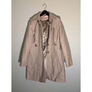 May include: A beige trench coat hanging on a black hanger. The coat has a classic design with a notched collar, button closures, and a matching belt. The interior lining is a satin-like material.