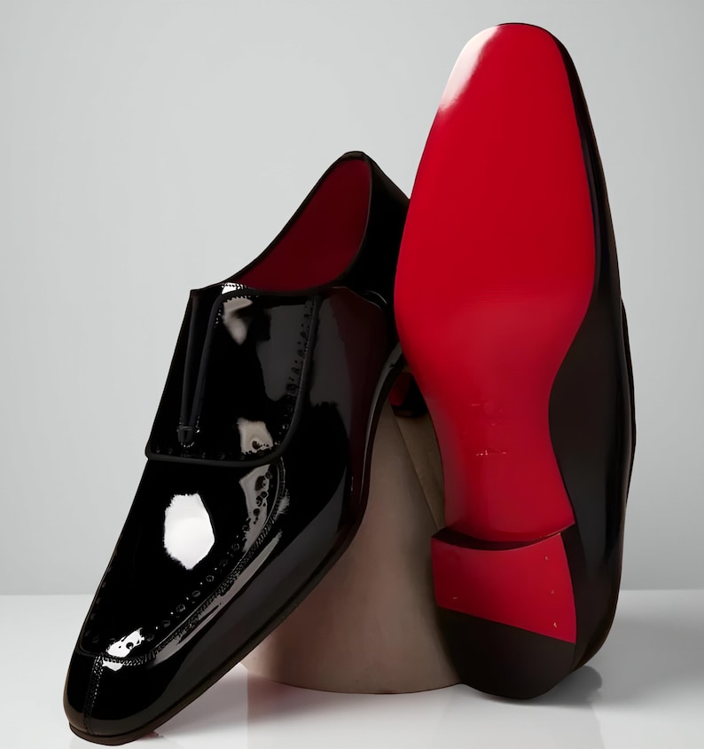 May include: Black patent leather dress shoes with a glossy finish. One shoe is upright, showcasing the design, while the other reveals a vibrant red sole. The shoes have a classic, formal style, suitable for special occasions.
