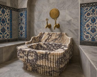 May include: A marble sink with a unique design, featuring a patterned surface and a fluted base. The sink is set against a backdrop of gray tiles and decorative blue and white floral tiles. Brass faucets and a round plate are mounted on the wall.