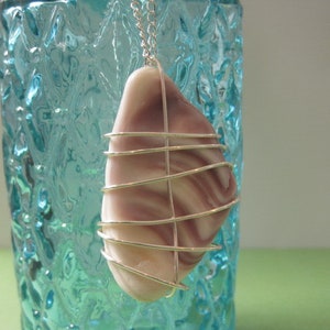May include: A silver wire wrapped around a purple and white seashell pendant. The pendant is hanging from a silver chain.