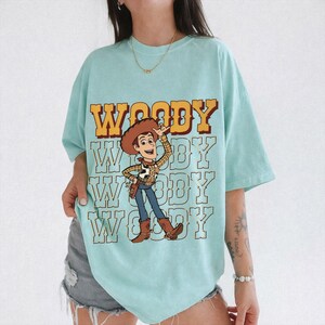 Pode incluir: Uma caneca de cer&acirc;mica branca com uma al&ccedil;a preta e o texto "But First, Coffee" em negrito preto. A caneca est&aacute; sobre um fundo desfocado. A caneca tem aproximadamente 10 cm de altura.