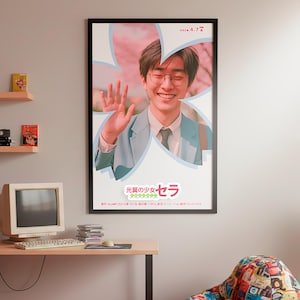 Pode incluir: Um poster emoldurado com uma pessoa sorrindo com óculos, acenando. O poster tem texto japonês e um design floral. O quarto inclui uma mesa com um computador vintage, uma cadeira de saco e prateleiras decorativas.