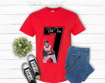 Puede incluir: Camiseta roja con un número 7 negro y una imagen de un jugador de béisbol. El texto "Pink Fizz Custom Designs" está en el número.