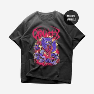 May include: Dark grey t-shirt with a vibrant illustration of a purple werewolf wearing a red plaid shirt, with skulls and the word "CARNIFEX". The brand name "MOSHPIT APPARELS" is also visible on the shirt.