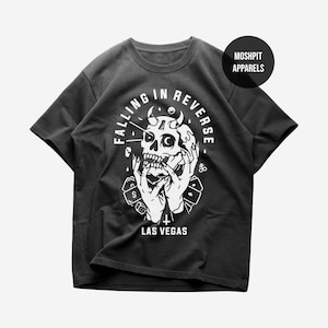 May include: Dark grey t-shirt with a white graphic of a skull with horns, hands, and the text "FALLING IN REVERSE" in a circular design. The text "LAS VEGAS" is below the graphic. A circular logo reads "MOSHPIT APPARELS".