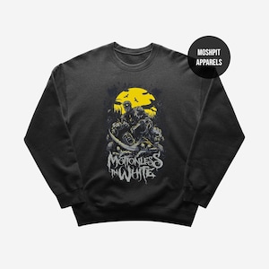 May include: Black crewneck sweatshirt featuring a yellow and black graphic of a skull-themed design with the text "MOTIONLESS IN WHITE". The sweatshirt has a round neckline and long sleeves. The brand name "MOSHPIT APPARELS" is printed on a black circle.