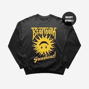 May include: Black crew neck sweatshirt with a yellow graphic. The graphic features the word "Beartooth" above a smiling sun with the word "Sunshine!" below. The brand name "Moshpit Apparels" is in a black circle.