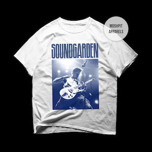 Puede incluir: Camiseta blanca con una imagen azul y blanca de un guitarrista en el escenario. La palabra "SOUNDGARDEN" está impresa en letras azules grandes encima de la imagen. La camiseta tiene cuello redondo y mangas cortas.