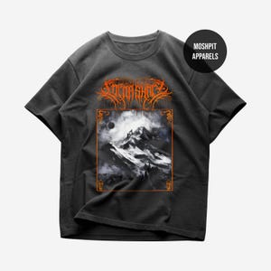 Puede incluir: Camiseta gris oscuro con un diseño de paisaje montañoso, borde naranja y texto. La camiseta tiene mangas cortas y cuello redondo. El texto "MOSHPIT APPARELS" está en la parte superior derecha.