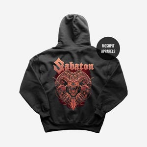 Könnte beinhalten: Dunkelgrauer Kapuzenpullover mit einem roten und orangefarbenen gehörnten Schädelmotiv und dem Wort "Sabaton". Das Design befindet sich auf der Rückseite. Ein schwarzer Kreis rechts trägt den Text "MOSHPIT APPARELS".
