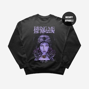 May include: Dark gray sweatshirt featuring a graphic of a woman with a lion headdress, a triangle with an eye, and the text "BRING ME THE HORIZON". The design includes purple roses and accents. The brand name "MOSHPIT APPARELS" is also visible.