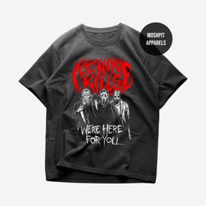 May include: Dark grey t-shirt with a graphic of three horror movie characters. The word "Killed" is in red above the characters, and the text "We're Here For You..." is below. The shirt has a crew neck and short sleeves.