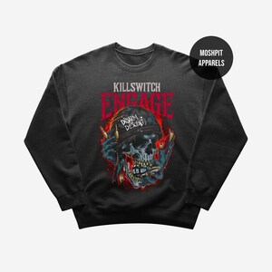 May include: Dark gray sweatshirt featuring a skull graphic with the text "KILLSWITCH ENGAGE" in red. The skull wears a black bandana with "Disarm Descent" printed on it. The design includes flames and blue accents.