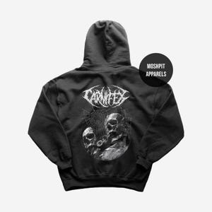 May include: Dark grey hooded sweatshirt with a white CARNIFEX band graphic and skull design. The sweatshirt has a drawstring hood and a kangaroo pocket. The brand name MOSHPIT APPARELS is printed on a black circle.