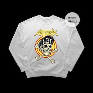 May include: White sweatshirt with a graphic of a skull wearing a black cap with the word "NOT" and crossed bones. The word "ANTHRAX" is above the skull in yellow letters with a red and yellow circle behind the skull.