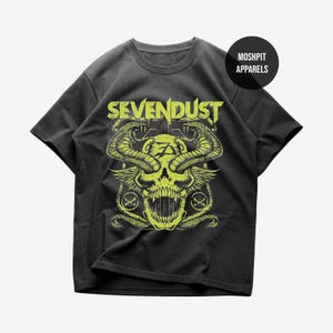 May include: Dark gray t-shirt featuring a neon green skull design with snakes, wings, and the band name "SEVENDUST". The shirt also has the text "MOSHPIT APPARELS" on a black circle.