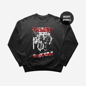 Może przedstawiać: Czarna bluza z okrągłym dekoltem z grafiką zespołu. Grafika zawiera słowo "Zombies" w kolorze czerwonym i "Para Los Punks" w kolorze czerwonym. Bluza ma długie rękawy i okrągły dekolt. Nazwa marki "Moshpit Apparels" znajduje się w czarnym okręgu.