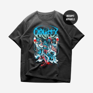 May include: Dark grey t-shirt with a graphic of zombie-like figures holding medical equipment and the word "CARNIFEX" in blue. The design includes red and blue accents, with the "MOSHPIT APPARELS" logo in a circle.
