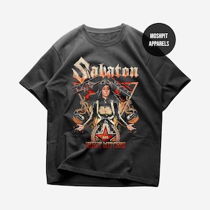 Könnte beinhalten: Dunkelgraues T-Shirt mit dem Bandnamen "Sabaton" in einer stilisierten Schriftart. Das Design zeigt eine Frau mit ausgestreckten Armen, einen roten Stern und die Worte "Night Witches". Ein "Moshpit Apparels"-Logo befindet sich oben rechts.