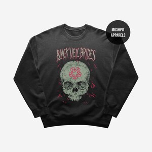 May include: Dark gray sweatshirt featuring a skull graphic with a pink and gray design. The text "BLACK VEIL BRIDES" is above the skull in pink lettering. The brand name "MOSHPIT APPARELS" is in a black circle in the upper right corner.