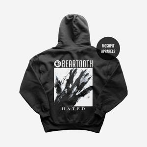 May include: Dark grey hoodie with the band name "BEARTOOTH" above a black and white abstract hand design. The word "HATED" is below the design. A black circle with "MOSHPIT APPARELS" is on the upper right.