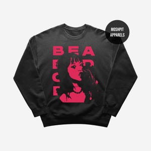 May include: Dark grey crew neck sweatshirt featuring a red graphic of a woman and the word "BEACH" in red block letters. The sweatshirt also has the text "MOSHPIT APPARELS" in a black circle.