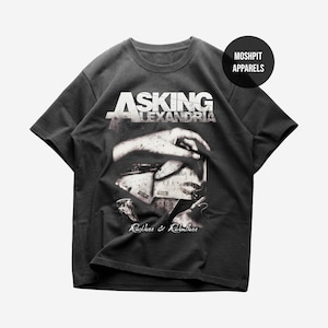 Puede incluir: Camiseta gris oscuro con el nombre de la banda "Asking Alexandria" en letras blancas. El gráfico en blanco y negro muestra una mano y las palabras "Reckless & Relentless". La camiseta tiene cuello redondo y mangas cortas.