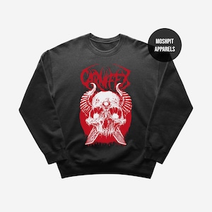May include: Black crew neck sweatshirt with a red graphic. The graphic features a skull with horns, a third eye, and crossed knives, set against a red circle. The word "CARNIFEX" is above the skull in red.