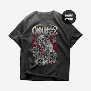 Può includere: T-shirt grigio scuro con un design grafico con un teschio, figure e la parola "CARNIFEX" in stile invecchiato. Il design incorpora accenti rossi e bianchi. La maglietta ha maniche corte e girocollo, con "MOSHPIT APPARELS" stampato in alto a destra.