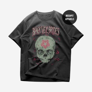 Könnte beinhalten: Dunkelgraues T-Shirt mit einem Totenkopf-Motiv, einem rosa Blumendesign auf der Stirn und dem Text "BLACK VEIL BRIDES" in Rosa. Das Shirt hat auch den Text "MOSHPIT APPARELS" in einem schwarzen Kreis.