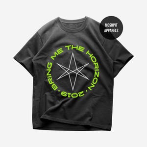 Puede incluir: Camiseta gris oscuro con un diseño circular verde neón que dice "BRING ME THE HORIZON 2019". Una estrella geométrica blanca está en el centro. La marca "MOSHPIT APPARELS" está en un círculo negro en la esquina superior derecha.