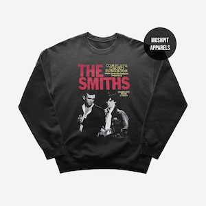 Op de afbeelding: Zwart sweatshirt met de bandnaam "The Smiths" in het rood en een zwart-wit afbeelding van twee mannen. De tekst "Complete Chord Songbook" en "Complete with Lyrics" zijn ook zichtbaar. De sweatshirt heeft een ronde hals en lange mouwen.
