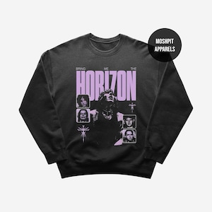 May include: Dark gray sweatshirt featuring the band name "Bring Me The Horizon" in lavender, with band member portraits. The sweatshirt has a crew neck and long sleeves. The brand name "Moshpit Apparels" is printed on a black circle.