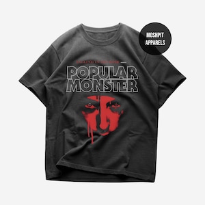 May include: Dark grey t-shirt with the white text "POPULAR MONSTER" and a red face graphic. The shirt also features the text "FALLING IN REVERSE" and the brand logo "MOSHPIT APPARELS".