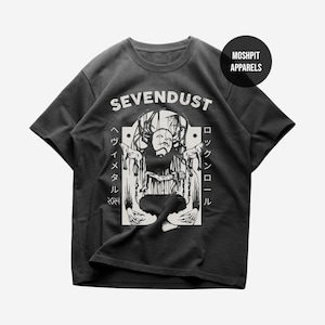 May include: Dark gray t-shirt featuring the band name "SEVENDUST" above a black and white graphic. The graphic depicts a figure with a mask and Japanese text on the sides. The shirt has a crew neck and short sleeves.
