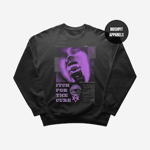 May include: Black crewneck sweatshirt with a purple graphic design. The design features a screaming face, the words "ITCH FOR THE CURE", an eye, and other text. The brand name "MOSHPIT APPARELS" is printed on a black circle.