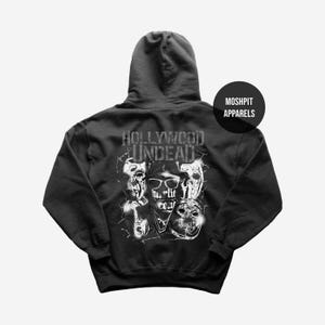 May include: Dark gray hoodie featuring a graphic of multiple masks and the text "HOLLYWOOD UNDEAD" in white. The hoodie also has the text "hurlie reav" and the brand name "MOSHPIT APPARELS".