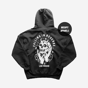 May include: Dark grey hoodie with a white graphic on the back. The graphic shows a skull with horns, hands, dice, and the text "FALLING IN REVERSE" and "LAS VEGAS". A black circle with the text "MOSHPIT APPARELS" is on the upper right.