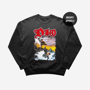 May include: Black crewneck sweatshirt featuring the band name "Dio" in red gothic lettering above a graphic of a demon figure and a person in water. The words "Holy Diver" are printed in red at the bottom of the graphic.