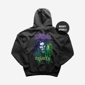 May include: Black hooded sweatshirt featuring a graphic of Rob Zombie with the text "ROB ZOMBIE DRAGULA" in purple and green. The sweatshirt has a drawstring hood and a kangaroo pocket. The brand name "MOSHPIT APPARELS" is printed on a black circle.