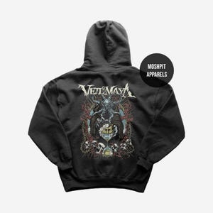 Op de afbeelding: Zwarte hoodie met de bandnaam "Veil of Maya" in het wit, boven een gedetailleerde afbeelding. De afbeelding bevat een figuur, schedels en een zandloper. Het merk "Moshpit Apparels" is op een zwarte cirkel gedrukt.
