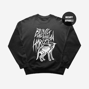 May include: Black crewneck sweatshirt with a white graphic featuring a skeletal wolf and the text "BRING ME THE HORIZON". The sweatshirt has a round neckline and long sleeves. The brand name "MOSHPIT APPARELS" is in a black circle.