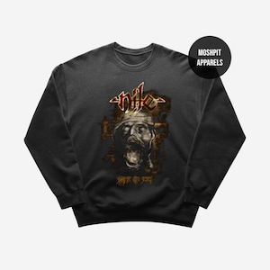 May include: Dark grey sweatshirt with a graphic of a screaming face and the word "nile" in red and gold. The text "worship the dead" is below the graphic. The sweatshirt has a crew neck and long sleeves, typical of a casual top.