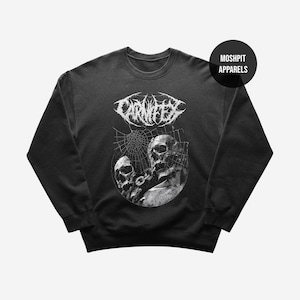 May include: Black crew neck sweatshirt with a white graphic. The graphic features the band name CARNIFEX above a circular design with two skulls and a spiderweb. The brand name MOSHPIT APPARELS is on the upper right.