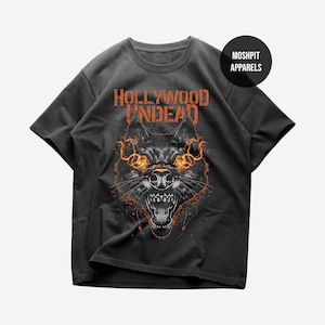 May include: Dark gray t-shirt featuring a snarling wolf graphic with orange flames and the text "HOLLYWOOD UNDEAD" in orange. The shirt also has a circular logo that says "MOSHPIT APPARELS".